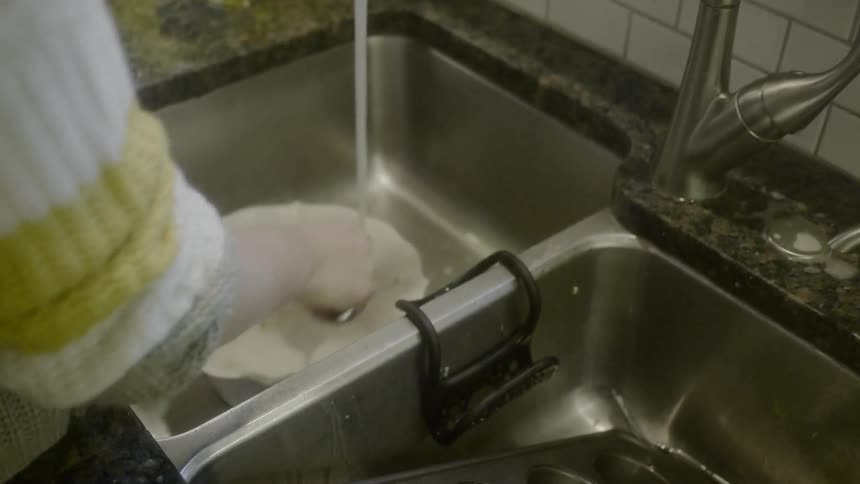 A woman places a bowl into a sink with running water to wash