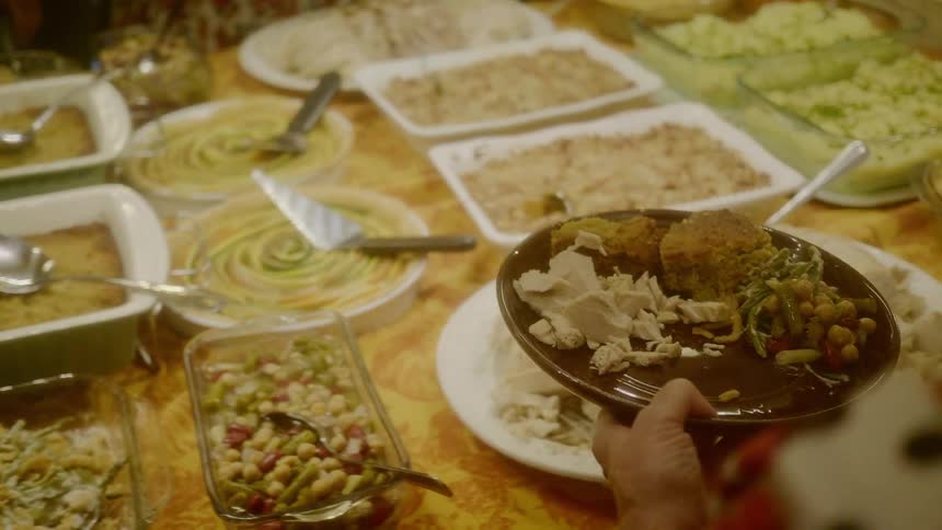 People walk around a table full of food and put it on their plates