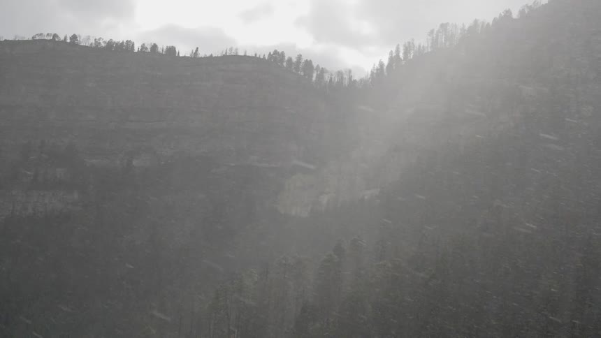 Snow falls in a forest with tall steeped mountains