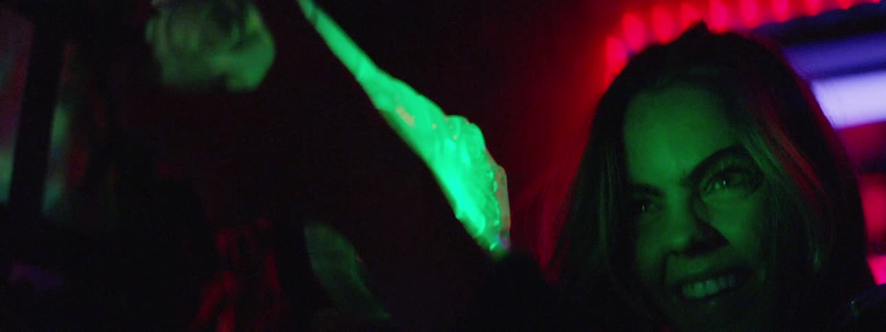 A woman smiles and appears excited as she aims a plastic laser tag gun in a dark room lit with flashing colored lights