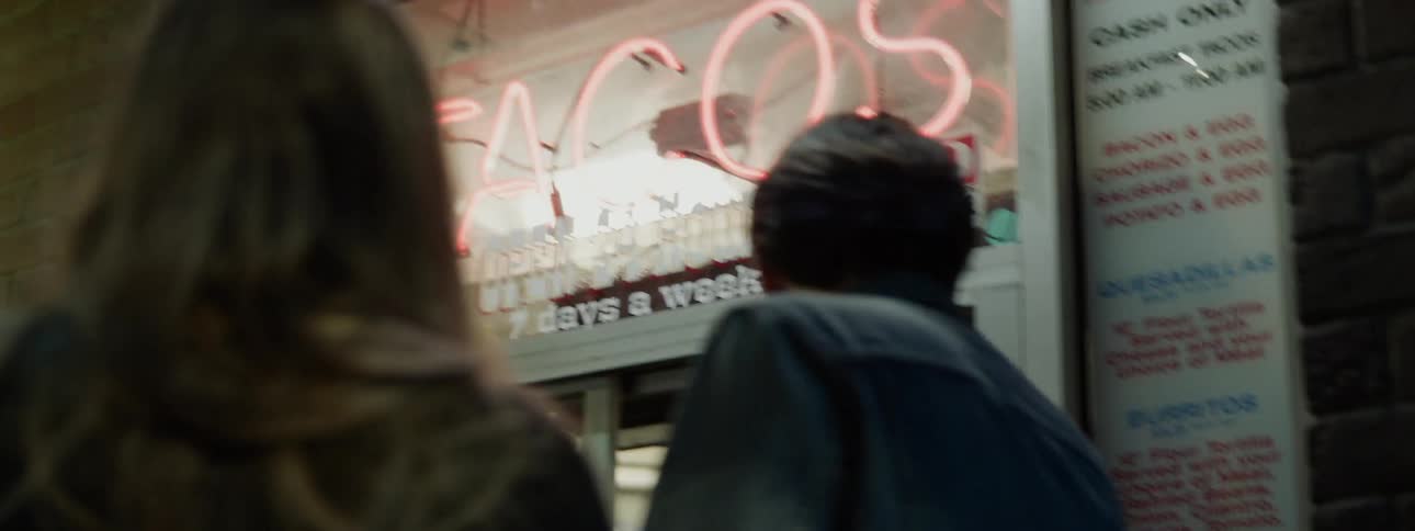 A man and a woman standing outside a taco shop at night