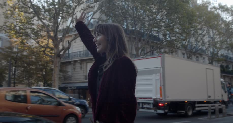 A woman walks along a busy street waving her hand