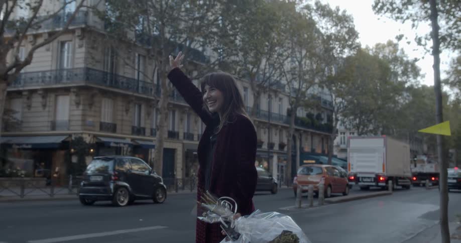 A woman is holding flowers and trying to catch a taxi