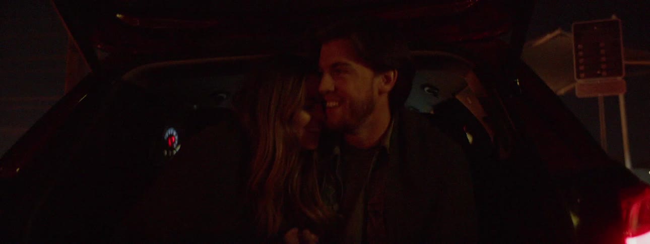 A man and woman cuddle in the back of a vehicle with the hatch open at night
