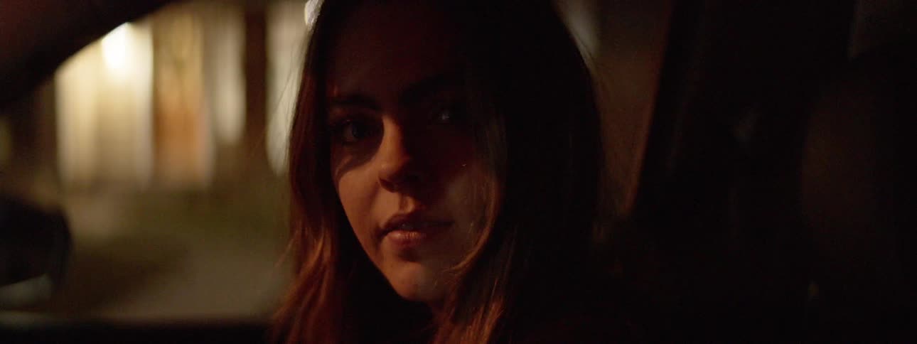A young woman sitting in the passenger seat at night looking into the camera
