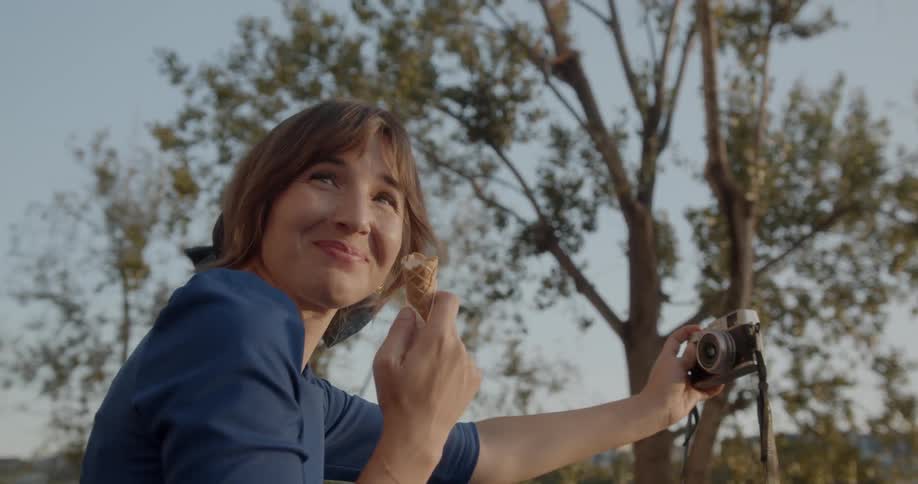 Woman takes a selfie with a camera while eating ice cream during daylight