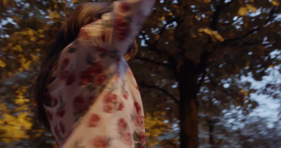 A woman in a floral dress spins under trees