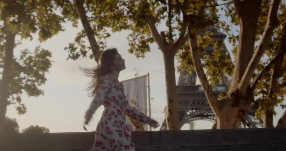 Woman in floral patterned dress walks in front of the eiffel tower on a sunny day