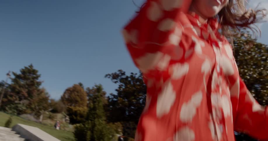 A woman in a red patterned shirt is jumping down the stairs outside of a large building