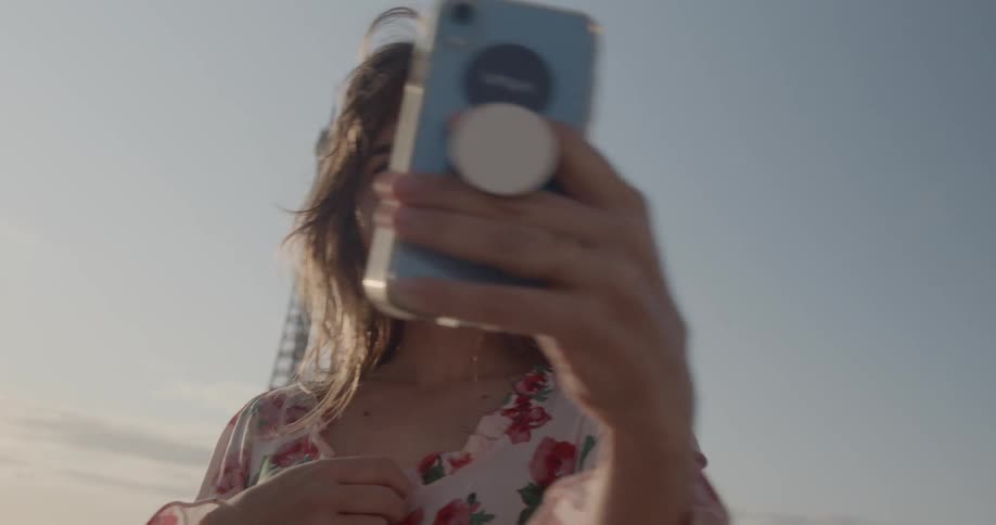 Woman smiles and takes a selfie with a smartphone in front of eiffel tower in paris during daylight