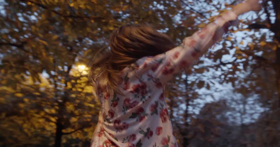 A woman spins around in a park at dusk