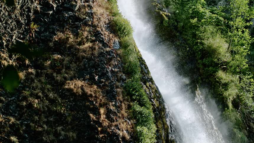 A narrow waterfall rushes down a lush green cliff
