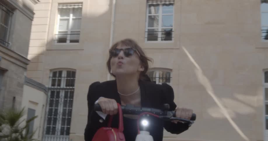 A young woman riding a scooter blows a kiss while passing by