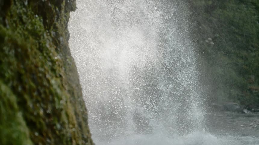 At the base of a waterfall falling over the side of a rocky cliff the water splashes forcefully into the river below