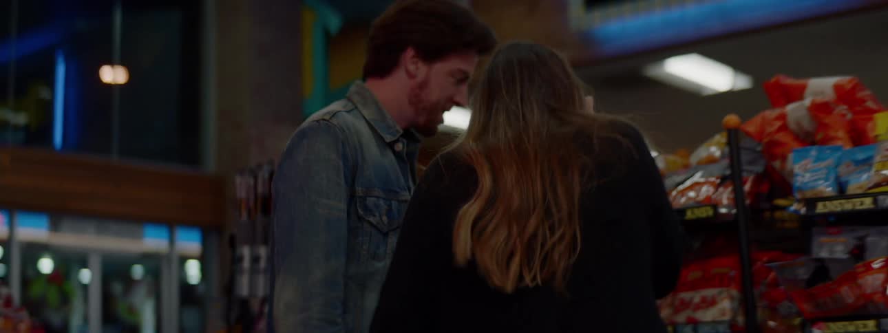 Couple holding hands picking up snacks at a liquor store at night