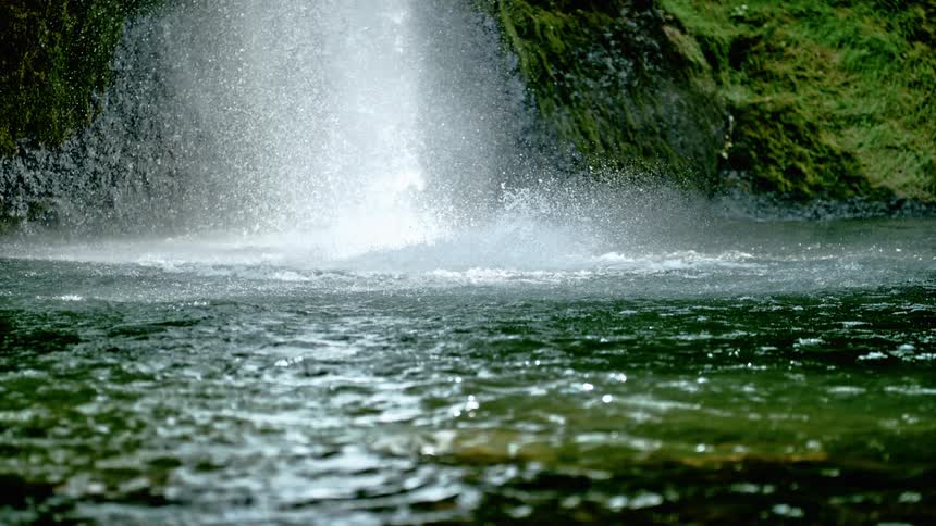 A waterfall crashes down the side of a hill in to the water below