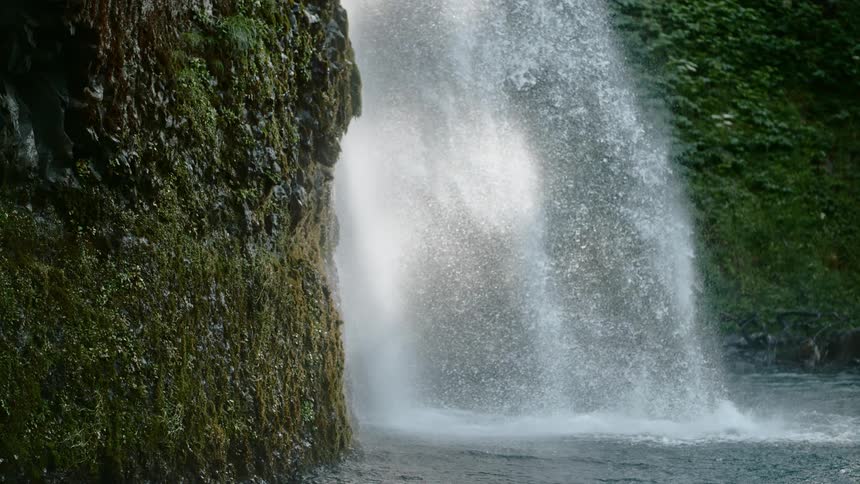 Water splashes and flows down a waterfall surrounded by green moss covered cliffs