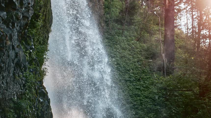 A waterfall flows over a rocky face in a forested area