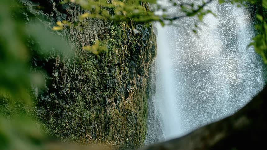 A powerful waterfall cascades down from the surface of a cliff covered in lush green vegetation