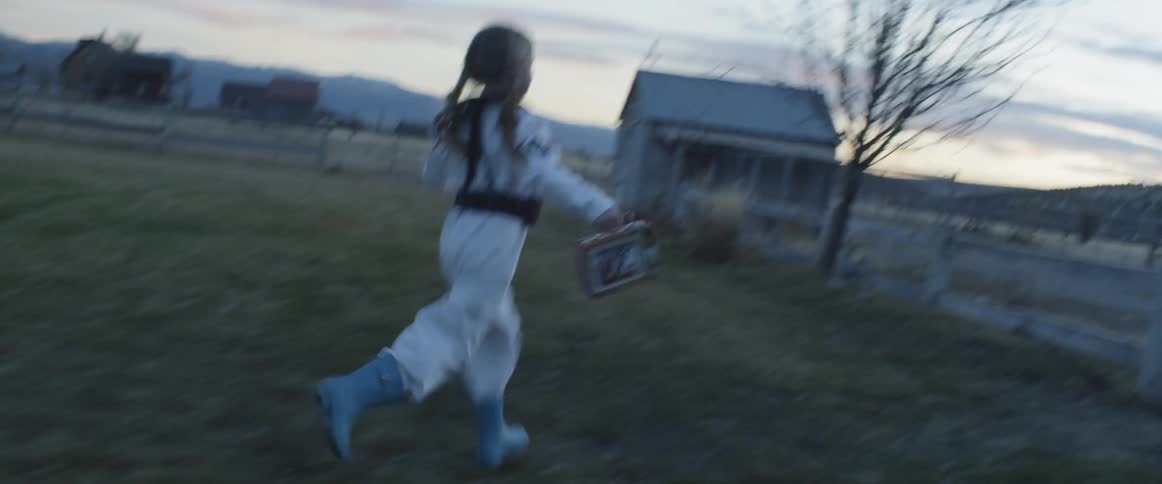 A child in an astronaut costume runs toward a barn