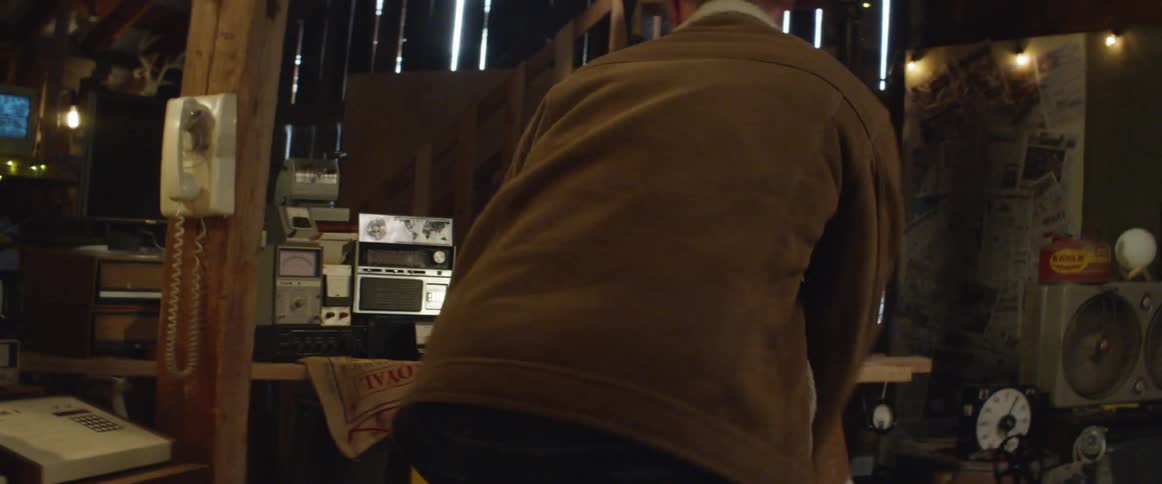 A child walking up to a man in a messy office work space in an outdoor barn