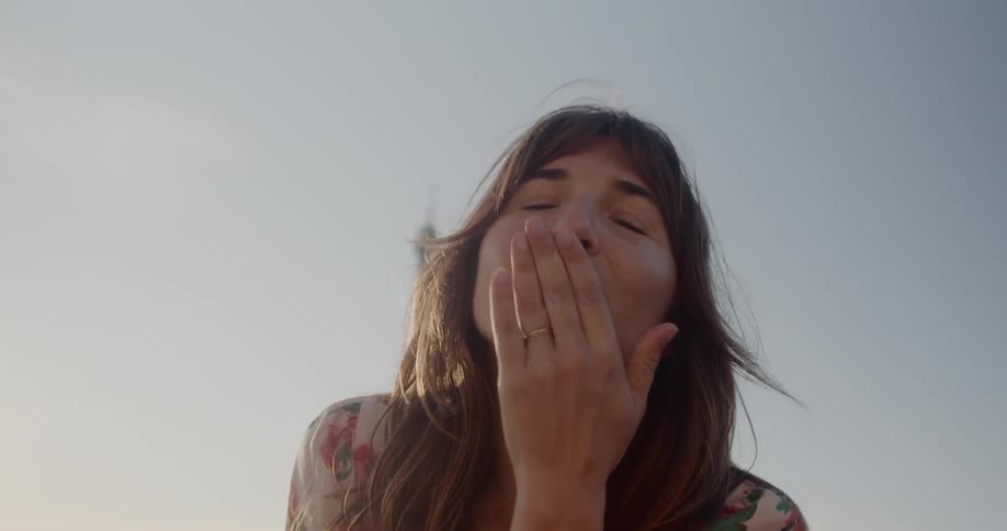 Woman stands in front of eiffel tower smiling and blows a kiss