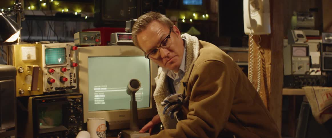 A radio announcer sits at a desk covered with monitors and other equipment