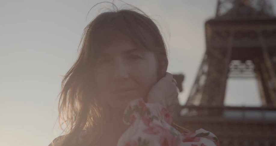 A woman stands in front of the eiffel tower brushing her hair back