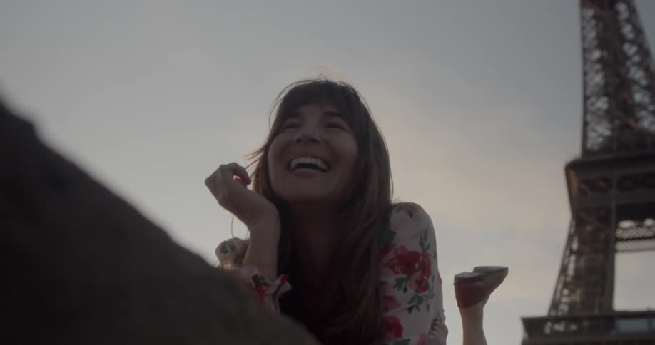 Woman lies down in front of the eiffel tower and laugh at sunset