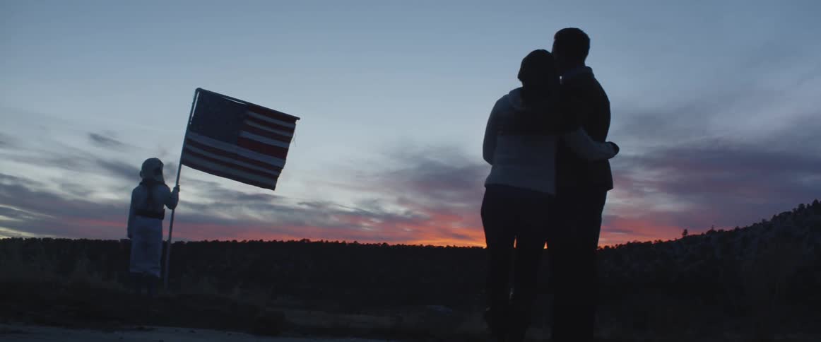 A child wearing astronaut suit holds americas flag being watched by his parents
