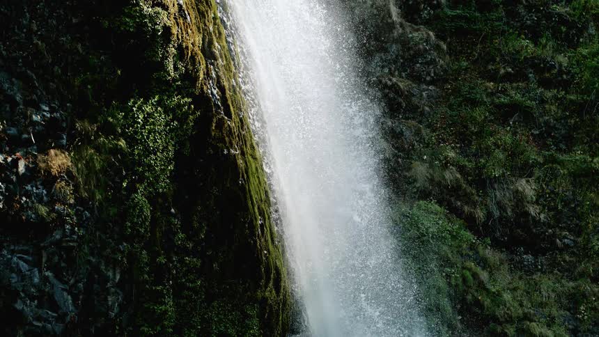 A waterfall streams over a rock face with moss growing on it