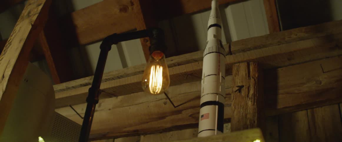 Illuminated light hangs from a pole inside a building next to a tall white rocket