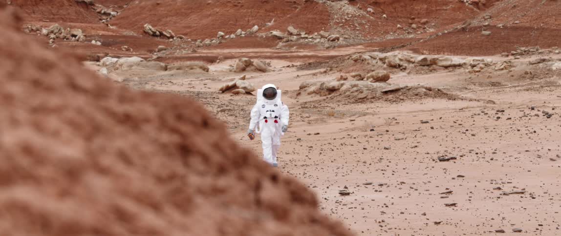 An astronaut walks along a sandy surface