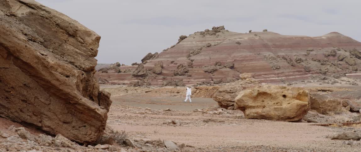 A person in a space suit walks through the desert