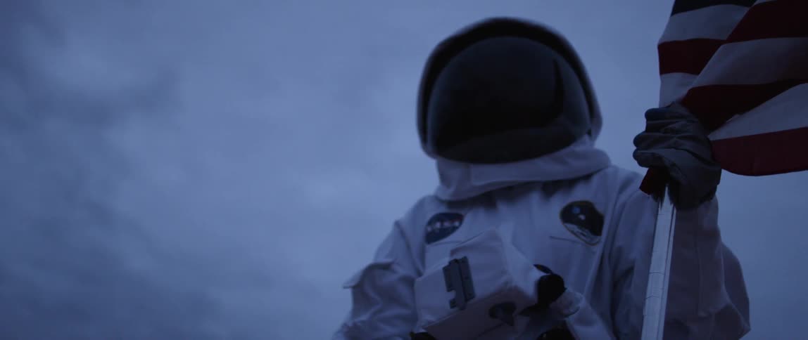 A person in an astronaut suit holds an american flag