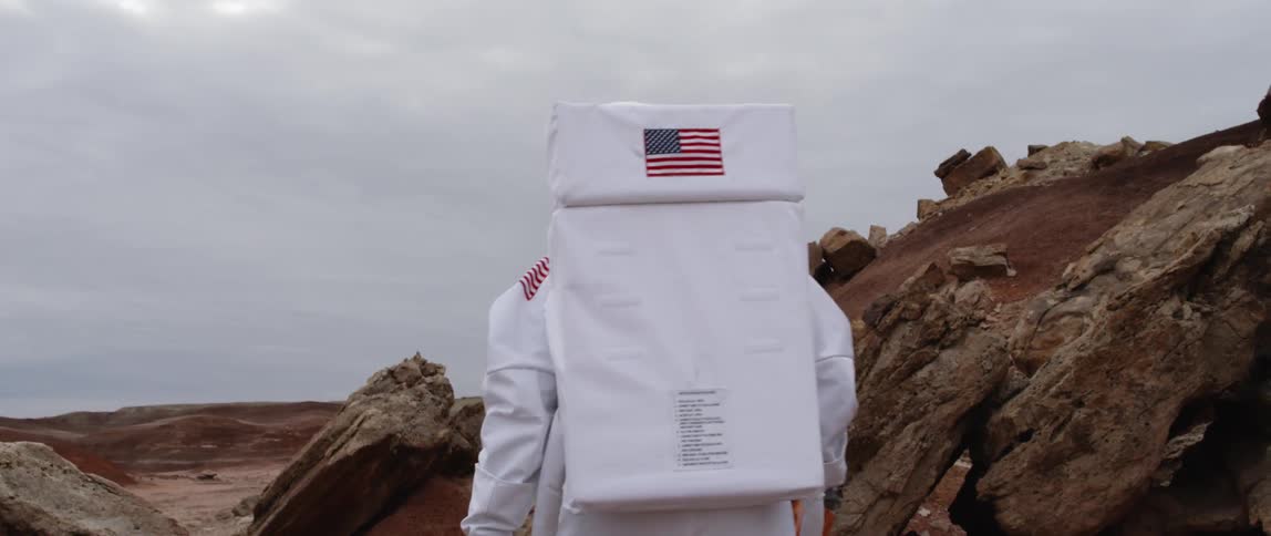 A person wearing an astronaut suit walks across a rocky terrain