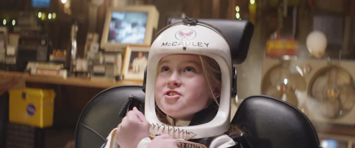 A young girl in an astronaut costume clutches a lunch box tightly