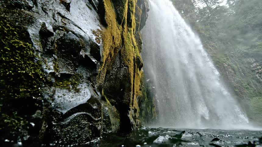 A waterfall crashes down the side of a mountain in to the water below
