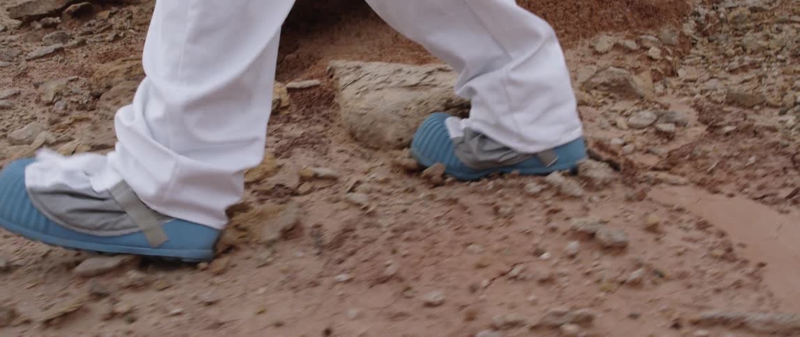 A person wearing special shoes walks over a rough rocky orange terrain
