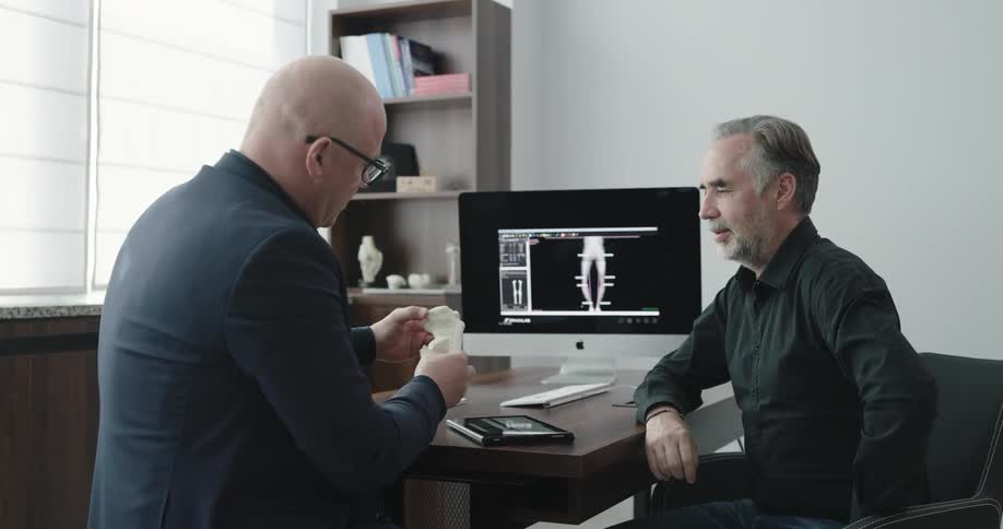 Doctor uses tablet and explains the kneecap to the patient in the office during daylight
