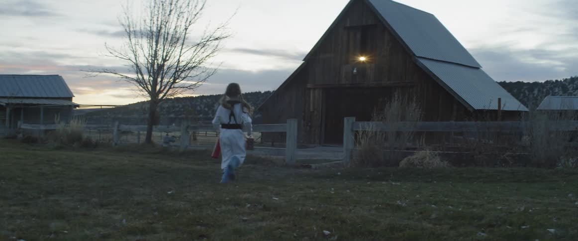 A young child in an astronaut costume runs to a barn