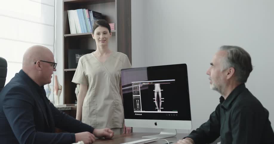 A patient sits and listens to a doctor and nurse as they show him information on a computer screen