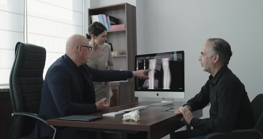A doctor and nurse discuss an x ray on a screen with a patient in an office