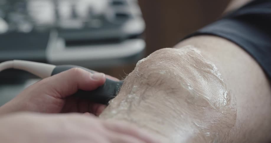 A person spreading gel on another persons knee using an ultrasound probe