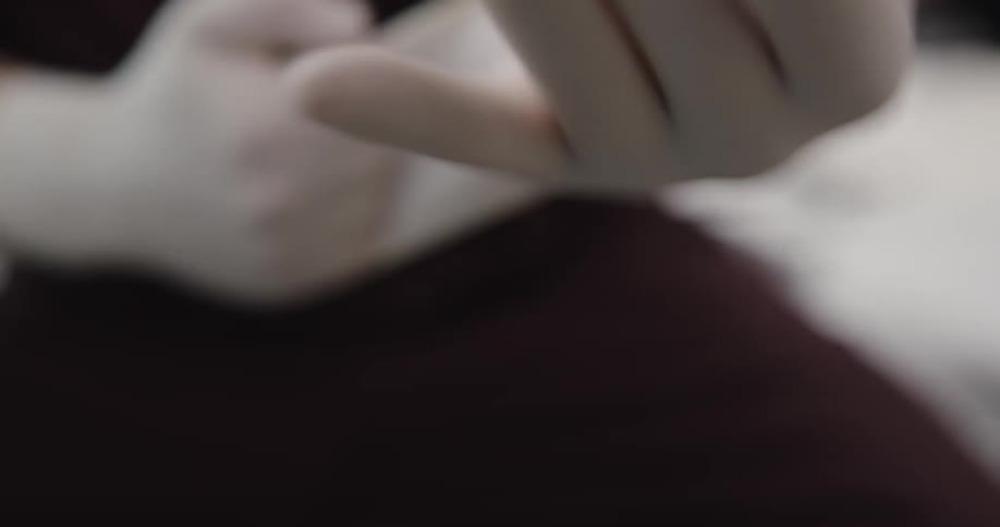Person putting on a second latex glove by putting their already gloved fingers into the fold of the glove pulling it up over their hand and adjusting both gloves so they fit comfortably