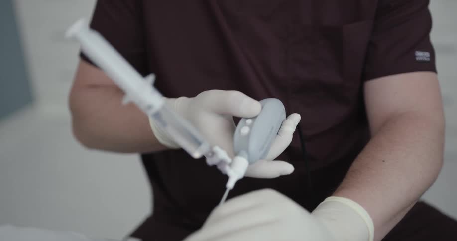 A male medical professional concentrates as he adjusts the angle of a large needle that he has placed in the knee of a patient