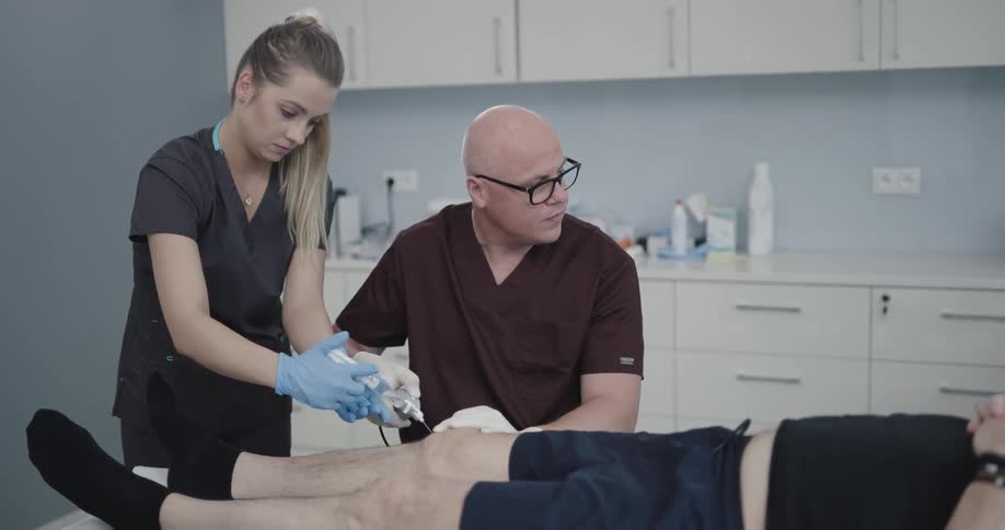 A male and female nurse working together to perform a medical procedure on a patients knee