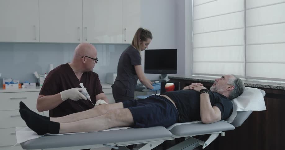 A middle aged male patient lays on a table while he receives a procedure from two health care professionals