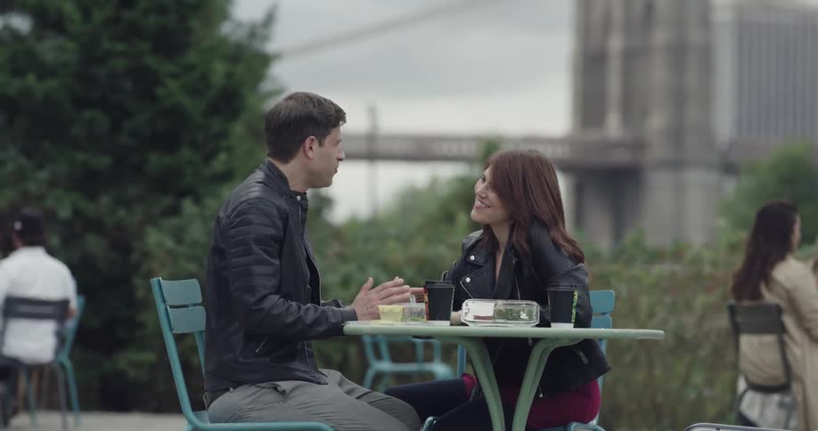 A man and woman are sitting at a table in an outdoor area with other people