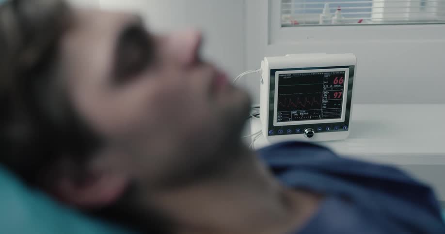 A white male is hooked up to a medical device while resting in a hospital bed